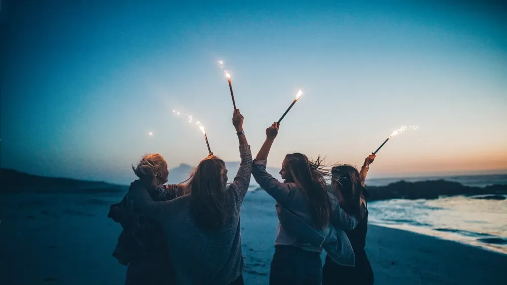 friends celebrating new years eve with sparklers on beach